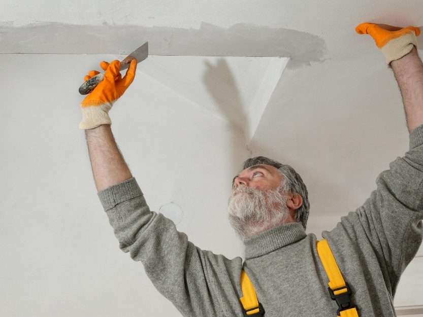Contractor repairing and finishing a damaged ceiling surface