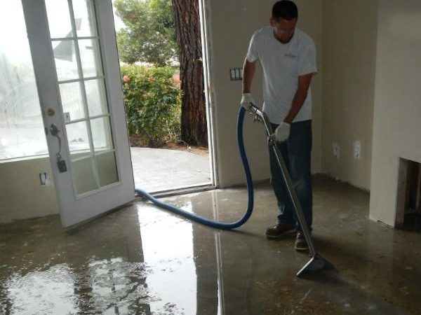 Technician removing standing water from a flooded interior floor with an extraction unit